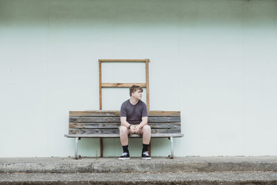 Teenage boy sitting alone on a wooden bench seat