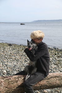 Young man embracing dog while sitting by lakeshore