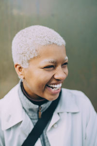 Happy young female looking away while standing against wall