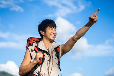 Low angle view of young man with arms raised against sky