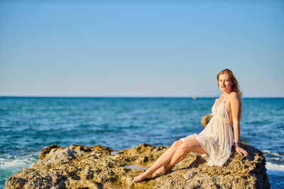 Portrait of beautiful woman sitting on rock against sea at beach