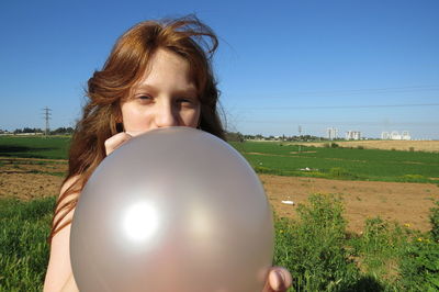 A redheaded girl inflates a balloon in a field