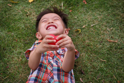 Happy boy with heart shape toy lying on field