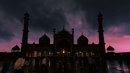 People in front of mosque against sky at dusk