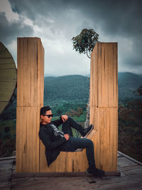 Full length of young man sitting against landscape