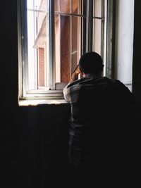 Rear view of man looking through window