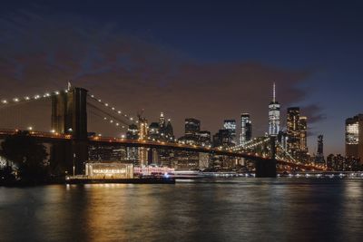 Illuminated bridge over river against sky in city at night