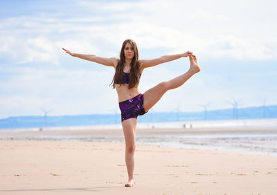 Full length portrait of young woman doing yoga at beach against sky