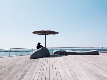 Silhouette man sitting under sunshade on shore against clear sky