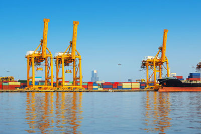 Cranes at commercial dock against clear blue sky