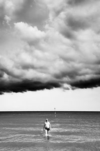 Man wading in sea against cloudy sky