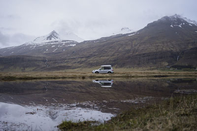 Car driving on gravel road with reflection in water, at dusk