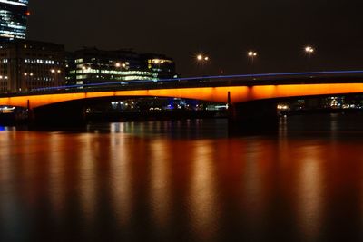 Illuminated bridge over river in city at night