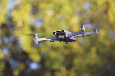 Low angle view of drone flying in front of trees