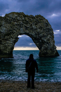 Silhouette man standing on rock by sea against sky