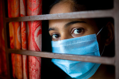 A bored asian young girl wearing a protective surgical face mask at looking through the window.