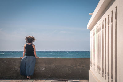 Rear view of woman standing at retaining wall against sky