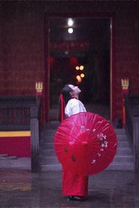 Rear view of woman with red umbrella walking at night