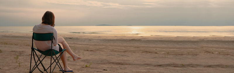 Backside solo asian woman relax and sit on beach chair with happiness and joyful in summer