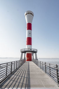 Lighthouse by sea against clear blue sky