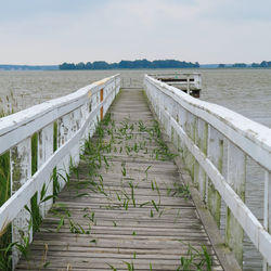 Wooden footbridge leading towards sea against sky