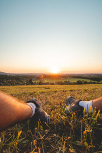 Low section of person on field against clear sky during sunset