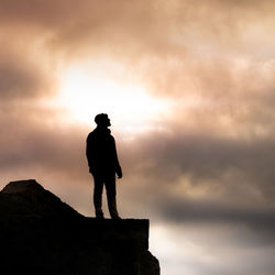 Silhouette man standing on mountain against cloudy sky during sunset