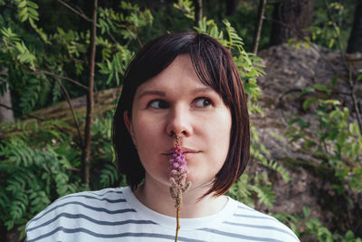 Smiling woman holding a flower in front of her lips and looking away. portrait of a happy, free