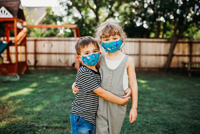 Brother and sister hugging outside while wearing homemade fabric masks