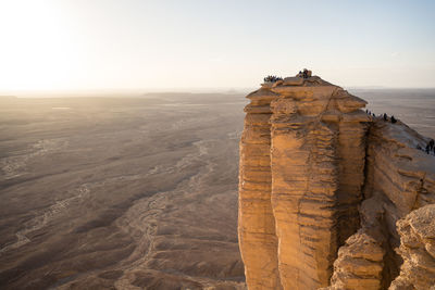 From above group of anonymous travelers contemplating colorful sundown while visiting the edge of the world in saudi arabia