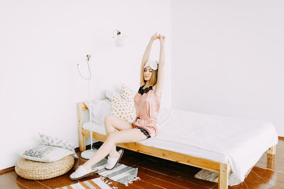 A happy cute girl in pink pajamas and a sleep mask wakes up and stretches on the bed at home