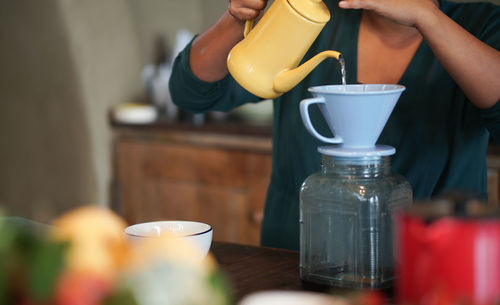 Midsection of person pouring coffee in cup on table