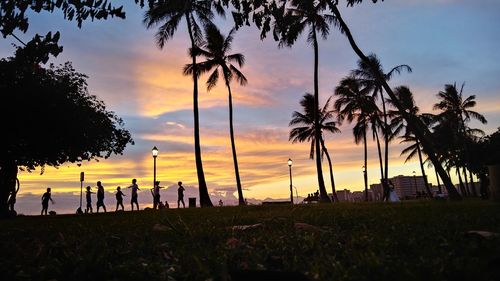 Silhouette people by palm trees against sky during sunset