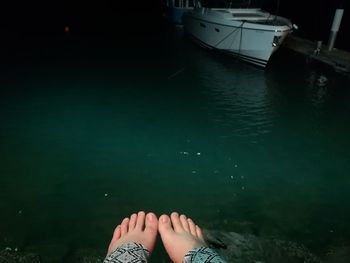 Low section of woman sitting by sea at night