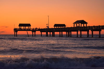 Silhouette pier on sea against orange sky