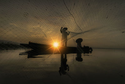 Men working on fishing net against sky during sunset
