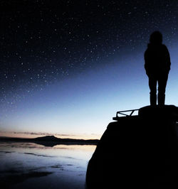 Silhouette man standing by sea against star field during sunset