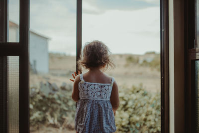 Rear view of girl standing by window at home