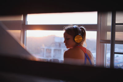 Rear view of woman listening music while sitting by window