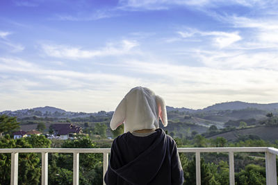Rear view of boy wearing mask while standing against landscape