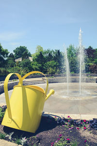  view of a spouting fountain with a giant yellow watering pail sculpture 