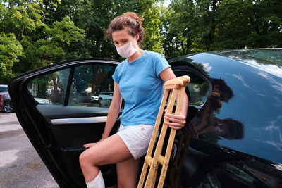 A woman with an injured leg gets into a car. orthopedic plaster, orthopedic crutches