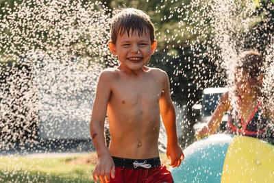 Water splashing on shirtless boy running in yard