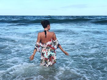 Rear view of woman standing at beach against sky