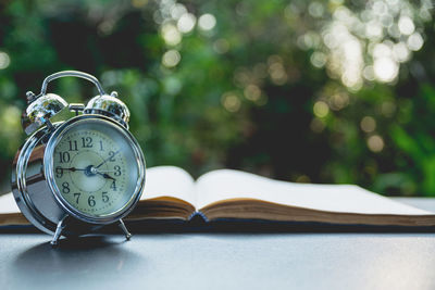 Close-up of alarm clock by open book on table