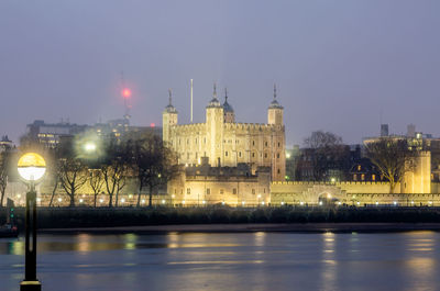 Illuminated buildings by river against sky at night