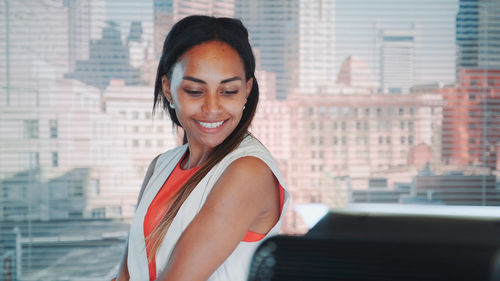 Portrait of a smiling young woman against buildings in city