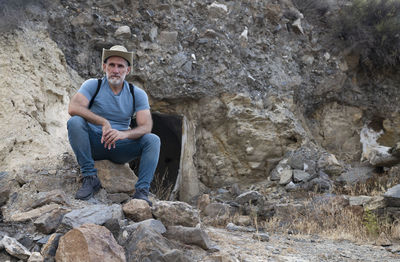 Portrait of adult man in cowboy hat and jean sitting in a rural area