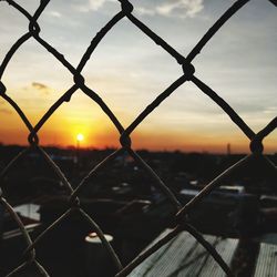 Close-up of chainlink fence against sky during sunset