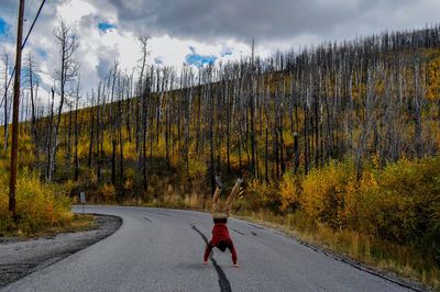 Rear view of man doing handstand on road amidst trees